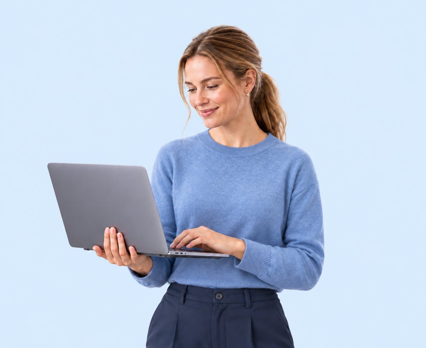 A woman in a blue jumper smiles at the laptop she is holding